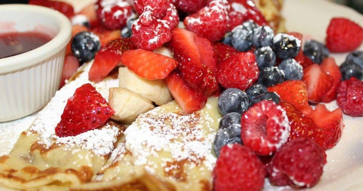 Two pancakes with powdered sugar, fruit, and syrup from Original Pancake House