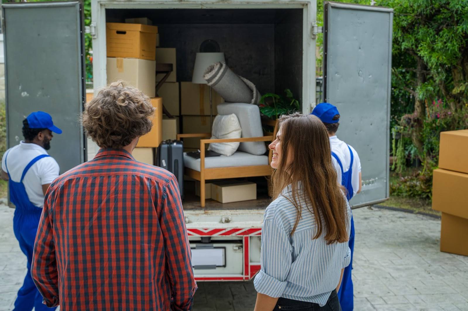 Young couple smiling as they watch Edgewater NJ movers load their belongings into a moving truck.
