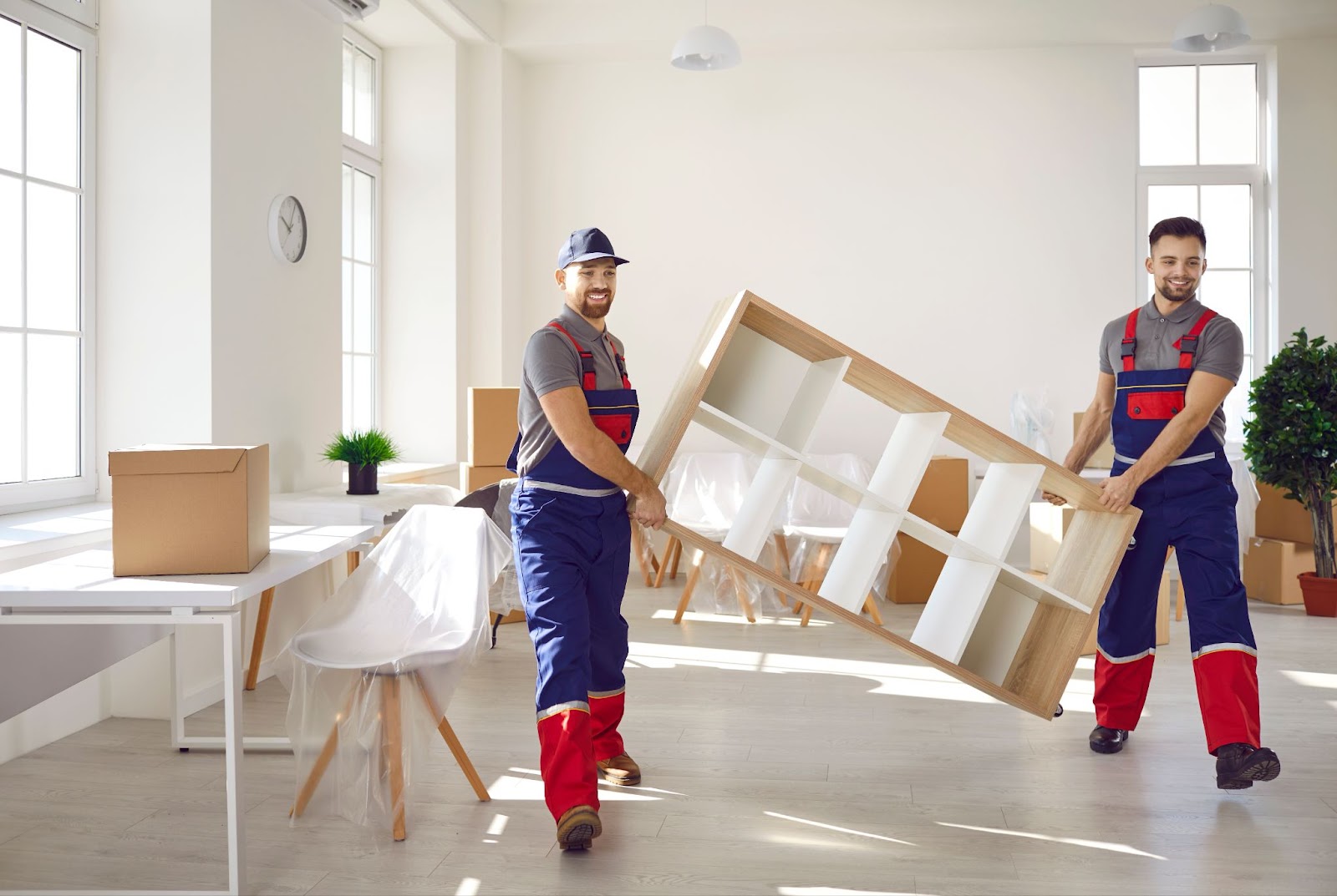 Two Franklin Lakes NJ movers in overalls smiling and carrying a shelf out of a home