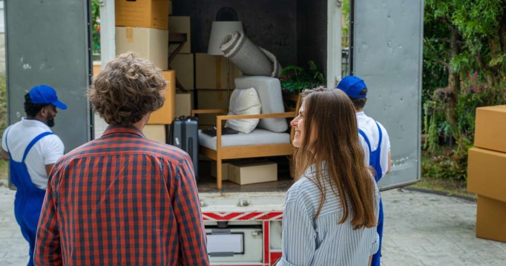 Happy couple smiling as Hasbrouck Heights movers load the moving truck. 
