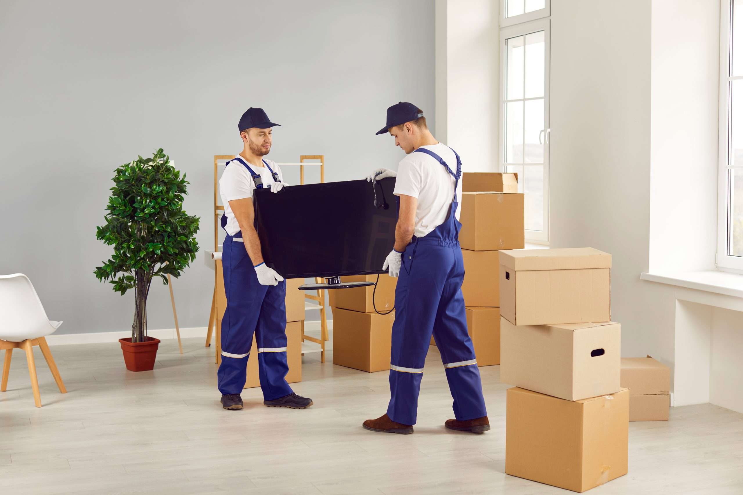 Saddle River movers in Blue overalls carrying a flat screen TV
