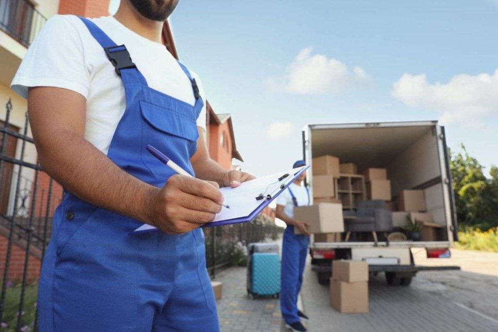 A Ridgefield mover with a clipboard standing in front of an open truck while another stands in the background with a box
