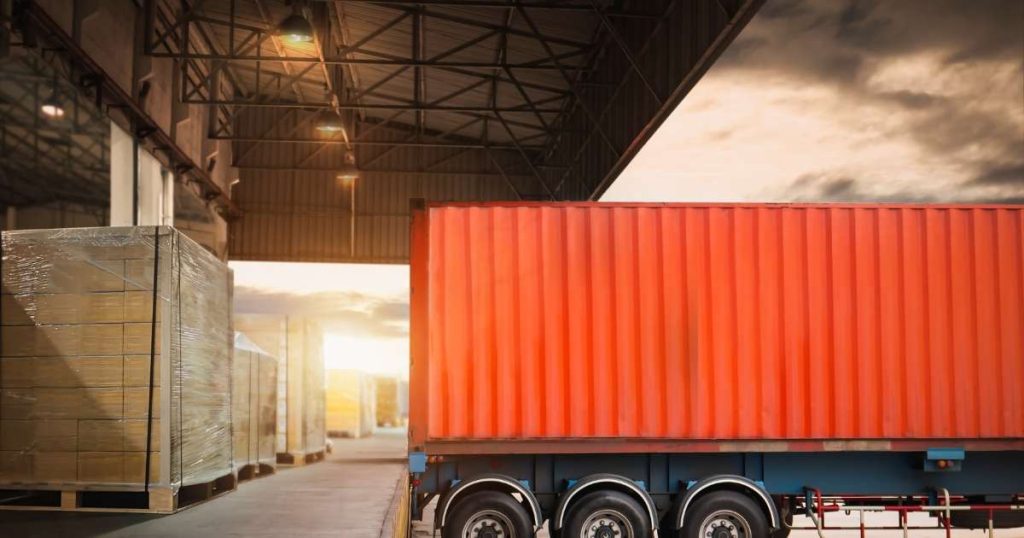 Red freight truck at an expansive warehouse picking up goods. 