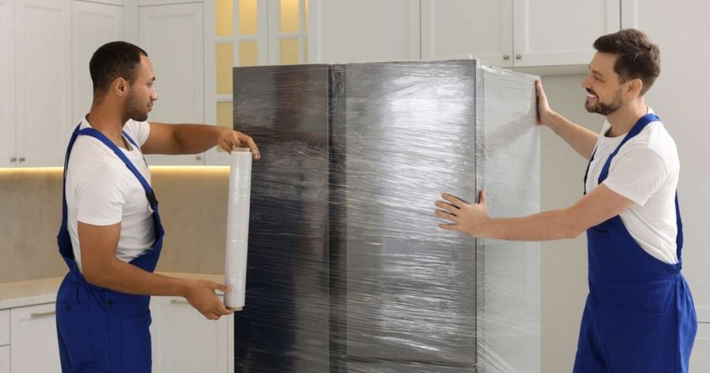 Two movers in Leonia transporting a wrapped and prepped fridge. 