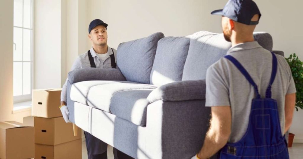 Skilled movers carrying a couch out to a specialized moving truck during a move.