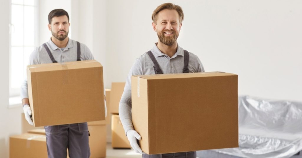 Two movers in Emerson NJ holding cardboard boxes in a living room