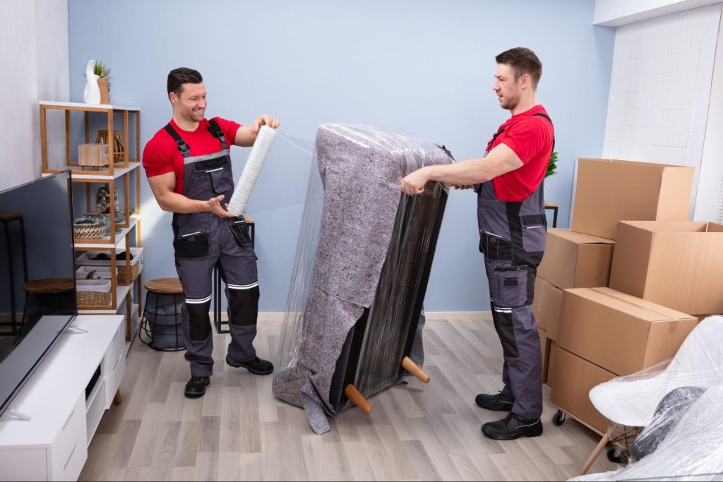 two movers wrapping a couch in plastic wrap