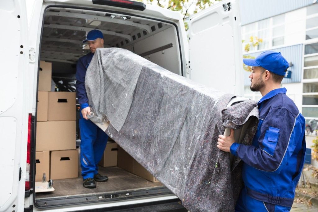 Two Montclair movers loading a couch wrapped in plastic wrap into the back of a van