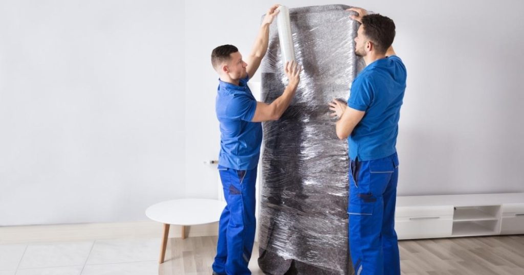 Two furniture movers with a Montclair moving company wrapping furniture in plastic wrap