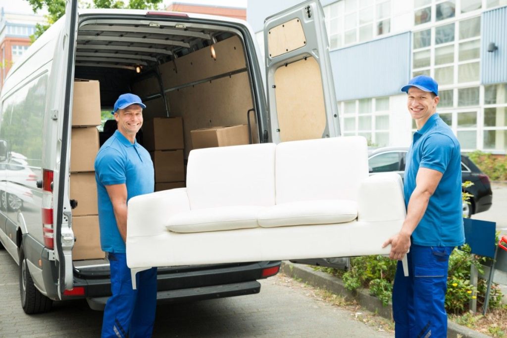 Two smiling Short Hills movers in blue polo shirts loading a white couch into the back of a van 