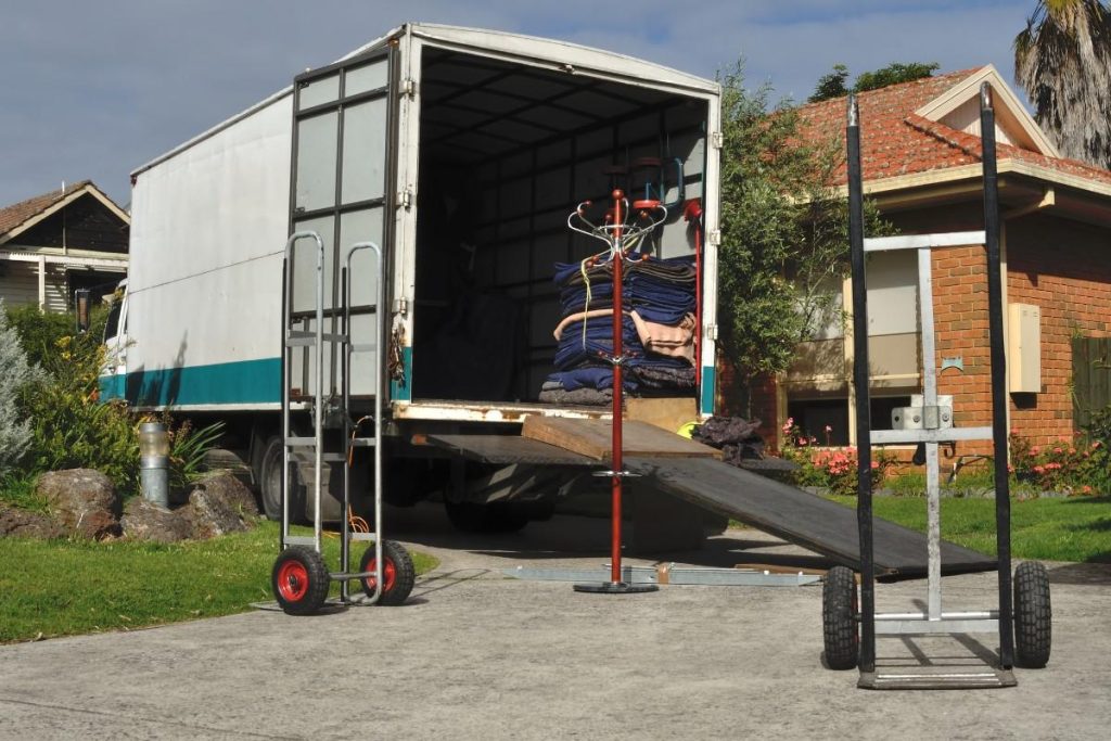 A moving van with the back open showing moving blankets and hand trucks in a drive way
